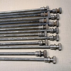 May include: A close-up of a set of silver metal spokes with threaded ends. The spokes are arranged in a row, with the threaded ends facing the viewer.