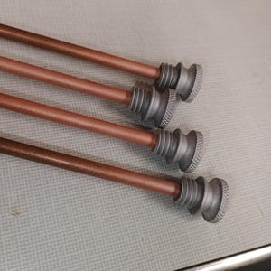 May include: Four straight, copper-colored rods arranged in parallel. Each rod features a silver-toned, cylindrical end cap with a textured, knurled grip pattern and a stepped, tiered design. The rods have a smooth, matte finish along their length.