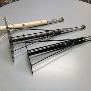 May include: Three metal table legs with adjustable height. The legs are made of black and white metal and have a triangular base.