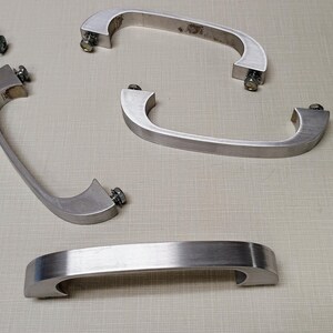 May include: Five silver metal cabinet door handles with a simple, curved design. The handles have a brushed finish and are attached with screws.