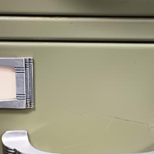 May include: Two metal file drawer labels with a silver finish and a white background. The labels are attached to a green metal file cabinet.