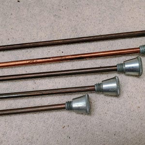 May include: Five metal rods with different lengths and a silver-colored tip on each end. The rods are arranged in a staggered pattern, with the longest rod at the top and the shortest rod at the bottom.