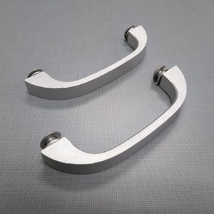 May include: Two silver-colored metal handles with rounded edges and a slightly textured finish. The handles have a simple, modern design and are suitable for a variety of applications.