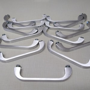 May include: A set of 12 silver-colored metal handles with a rounded, curved shape. The handles are arranged in a circular pattern, with the ends of each handle pointing towards the center.