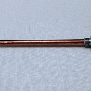May include: A copper-colored rod with a threaded metal end and a textured, circular cap. The rod appears to be approximately 12 inches long. The metal end is silver in color.