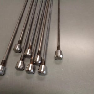 May include: A set of ten silver metal rods with rounded ends. The rods are arranged in a fan shape on a gray surface.