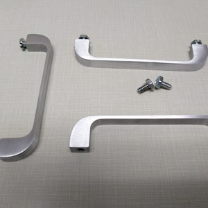 May include: Three silver cabinet handles with rounded edges and screw holes. Two handles are shorter and one is longer. Two screws are included.