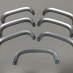 May include: Seven silver metal handles with screw-on attachments. The handles are curved and have a smooth finish.