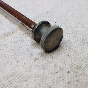 May include: A close-up of a wooden and metal tool with a round knob. The knob is silver and has a textured surface.