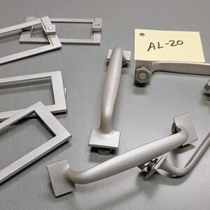 May include: A set of six silver-colored metal hardware pieces, including four rectangular plates and two handles. The handles have a curved shape and are labeled "AL-20".
