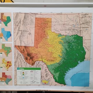 May include: A large wall-mounted pull-down map of Texas featuring a physical relief design. The map displays elevation gradients in green, yellow, and orange, with smaller inset maps on the left side showing various regional data and a legend at the bottom.