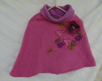 May include: A pink wool cape with a high collar and floral embellishments. The flowers are made of fabric and are in shades of pink, purple, and brown.