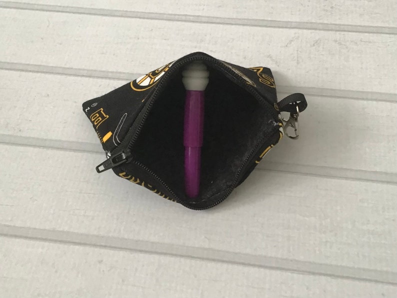 May include: A small black zippered pouch with a gold and white print of musical instruments. The pouch is open and a purple pen is inside.