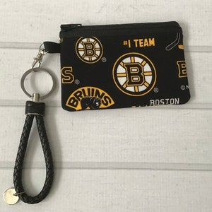 May include: Black zippered pouch with a black braided keychain. The pouch has a repeating pattern of the Boston Bruins logo, the words "#1 Team", "Bruins", and "Boston".