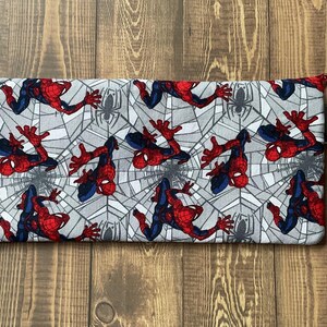 May include: A rectangular fabric pencil case featuring a repeating pattern of Spider-Man in red and blue suits against a gray spiderweb background. A matching hexagonal keychain with a red border and a metal lobster clasp is attached to the side.