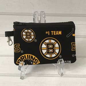 May include: Black zippered pouch with a repeating pattern of the Boston Bruins logo, the words "#1 TEAM" and "BOSTON". The pouch has a black zipper and a silver clip.