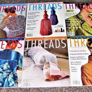 May include: A collection of six "Threads" magazines, each featuring a different cover image. The covers showcase sewing projects, including jackets, quilts, and various garment designs. The magazines are stacked on a neutral surface.