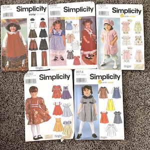 May include: Five different Simplicity sewing patterns for children's clothing. The patterns are for dresses, skirts, and tops. The patterns are all in different colors and styles. The patterns are all for different sizes. The patterns are all for different ages. The patterns are all for different occasions.