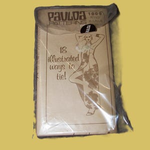 May include: A vintage Paula Patterns sewing pattern packet, sealed in plastic. The packet features an illustration of a woman in a floral dress and the text "18 illustrated ways to tie!" The packet is tan with black text.