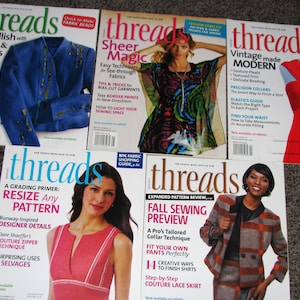 May include: A collection of "Threads" magazines, each featuring colorful cover designs. The covers showcase sewing projects, fashion, and techniques, with titles like "Sheer Magic" and "Fall Sewing Preview."