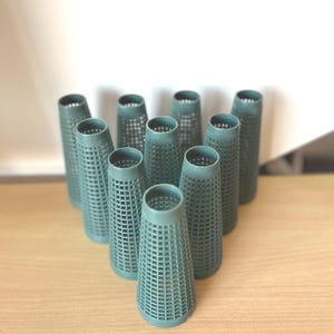 May include: A collection of teal-colored, cone-shaped objects with a grid-like pattern. The objects are arranged on a light brown wooden surface. The cones have a cylindrical top and a wider base, with a hollow interior.