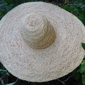 May include: A large, wide-brimmed straw hat with a woven texture. The hat is light beige in color and has a slightly rounded crown.
