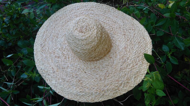 May include: A large, wide-brimmed straw hat with a woven texture. The hat is light beige in color and has a slightly rounded crown.