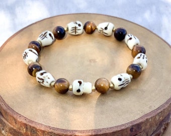 May include: A bracelet made of white skull beads and brown tiger's eye beads. The bracelet is displayed on a wooden stand.