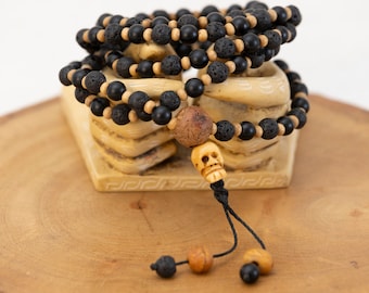 May include: A black and brown beaded necklace with a skull charm. The necklace is made of lava rock and wood beads and is displayed on a wooden stand.