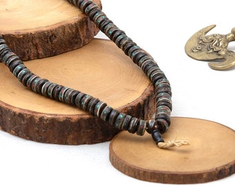 May include: A dark brown wooden mala necklace with turquoise accents, displayed on wooden rounds. The necklace is accompanied by two small brass ornaments.