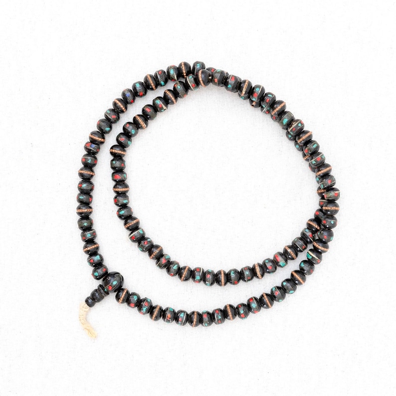Puede incluir: Un collar de cuentas negras con acentos rojos y verdes. Las cuentas son peque&ntilde;as y redondas, y el collar est&aacute; enhebrado en un cord&oacute;n delgado.
