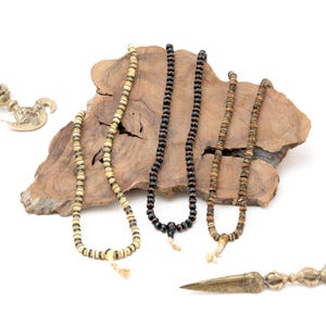 Puede incluir: Tres collares de cuentas con cuentas de diferentes colores, exhibidos sobre una superficie de madera. Los collares est&aacute;n hechos de madera y tienen una variedad de colores, incluyendo negro, marr&oacute;n y blanco.