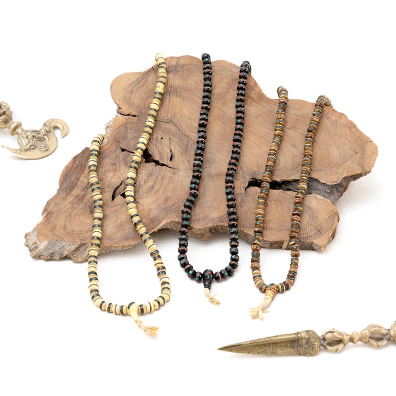 Puede incluir: Tres collares de cuentas con cuentas de diferentes colores, exhibidos sobre una superficie de madera. Los collares est&aacute;n hechos de madera y tienen una variedad de colores, incluyendo negro, marr&oacute;n y blanco.