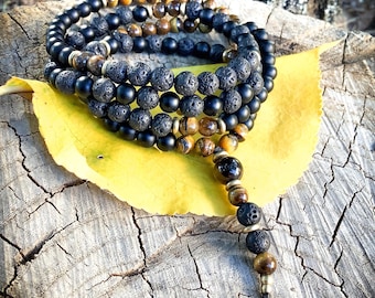 May include: A stack of beaded bracelets featuring black, brown, and gold beads. The bracelets are made of lava rock, tiger's eye, and onyx beads. The bracelets are displayed on a yellow leaf and a weathered wooden surface.
