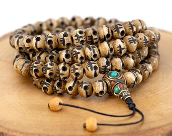 May include: A brown wooden mala with skull-shaped beads and a turquoise and red stone tassel. The beads are engraved with symbols.