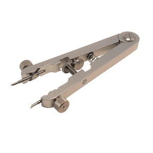 May include: A silver watch band tool with a spring-loaded mechanism and two adjustable pins. The tool is used to remove and install watch bands.