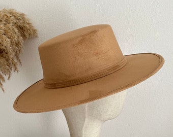 May include: A wide-brimmed brown felt hat with a flat top and a thin band around the crown. The hat is displayed on a wooden hat stand.