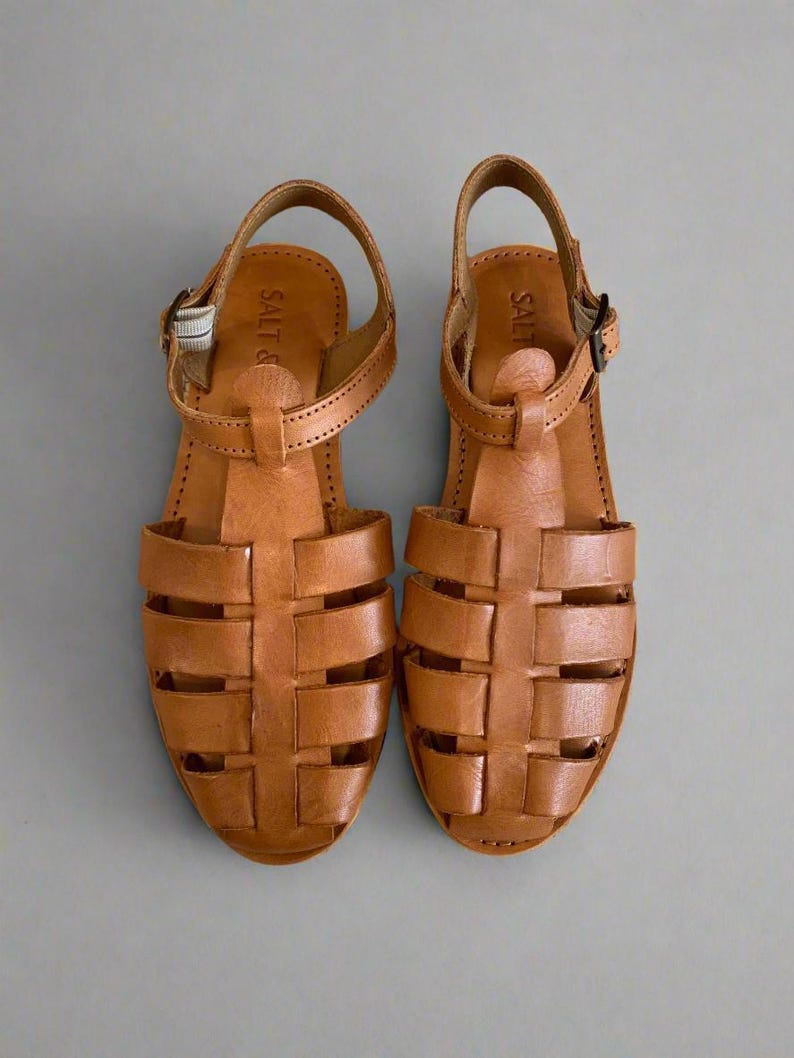 May include: A pair of brown leather sandals with a woven design. The sandals have a buckle closure and the brand name "Salt &" is visible on the strap.