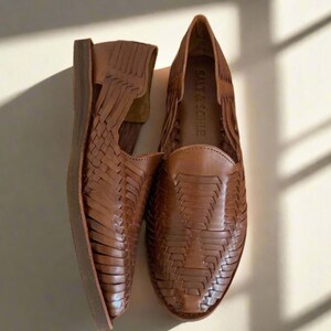 May include: A pair of brown leather woven sandals with a cut-out design. The sandals have a woven leather upper and a leather sole. The brand name "SALT & SORE" is visible on the inside of one sandal.