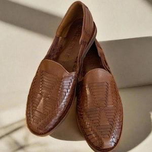 May include: A pair of brown leather woven flats with a woven pattern. The shoes have a pointed toe and a flat heel. The brand name "Salt & Shore" is visible on the insole of one shoe.