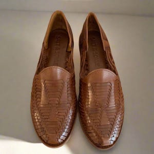 May include: A pair of brown leather woven slip-on shoes with the brand name "Salt & Sorel" on the inside of each shoe.