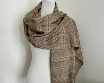 May include: A brown shawl with a geometric pattern and fringe. The shawl is draped over a white mannequin.