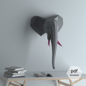 May include: A gray papercraft elephant head model with pink tusks. The model is mounted on a white wall. The model is a PDF template.