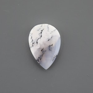 Op de afbeelding: Een witte en grijze traanvormige cabochon met zwarte dendritische insluitsels.