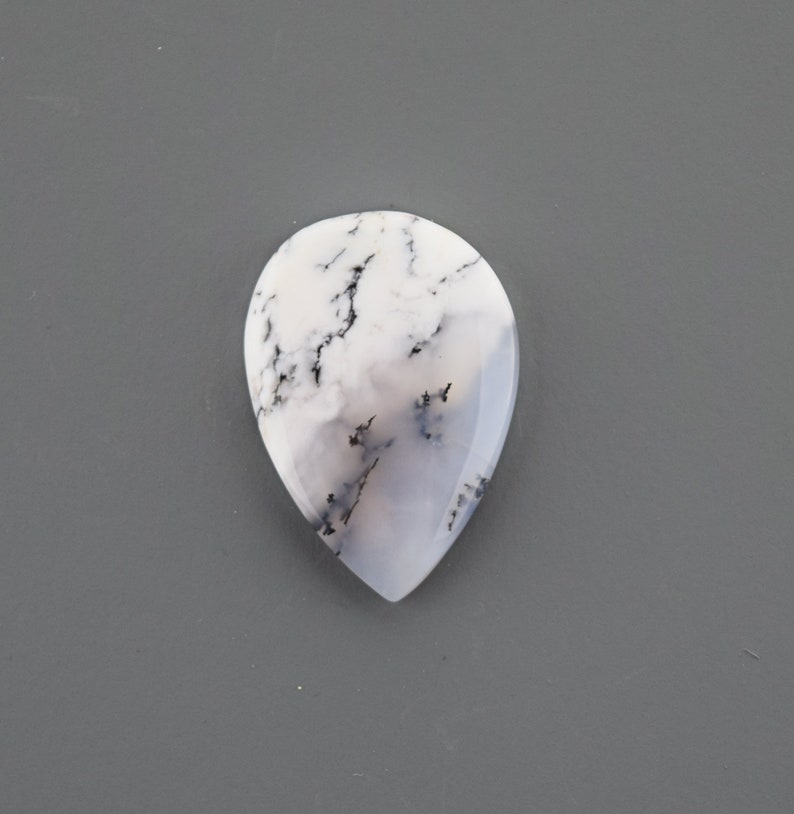 Op de afbeelding: Een witte en grijze traanvormige cabochon met zwarte dendritische insluitsels.