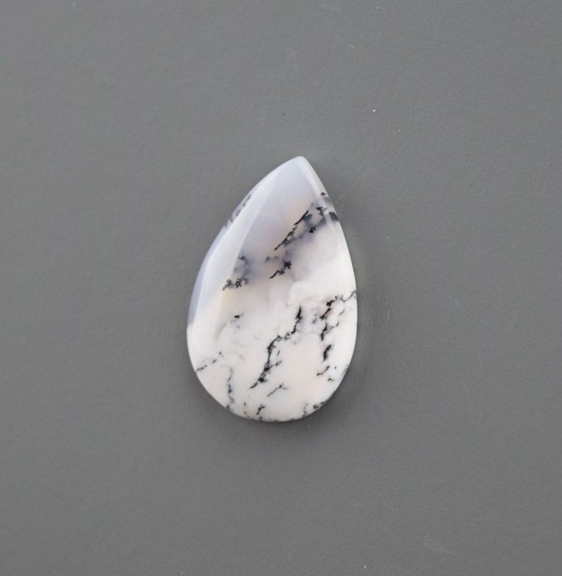Op de afbeelding: Een witte en zwarte dendritische opaal cabochon in een traanvorm.