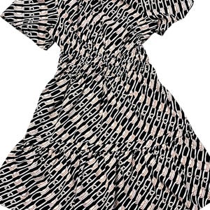Puede incluir: Vestido estampado en blanco y negro con mangas cortas y falda escalonada. El vestido presenta un dise&ntilde;o repetitivo en forma de cadena en blanco y melocot&oacute;n claro sobre un fondo negro. La cintura est&aacute; ce&ntilde;ida con el&aacute;stico.