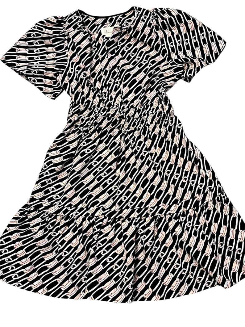 Puede incluir: Vestido estampado en blanco y negro con mangas cortas y falda escalonada. El vestido presenta un dise&ntilde;o repetitivo en forma de cadena en blanco y melocot&oacute;n claro sobre un fondo negro. La cintura est&aacute; ce&ntilde;ida con el&aacute;stico.