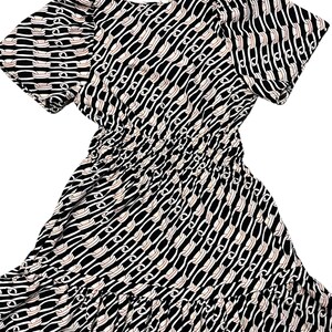 Puede incluir: Vestido estampado en blanco y negro con mangas cortas y cintura fruncida. El vestido presenta un dise&ntilde;o de eslabones de cadena repetidos en blanco y beige sobre un fondo negro. La falda tiene un dobladillo con volantes.