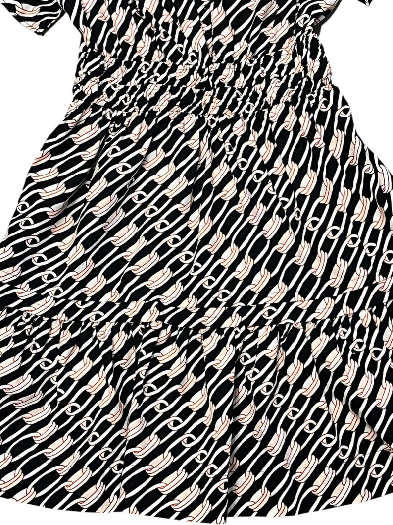 Puede incluir: Vestido estampado en blanco y negro con dise&ntilde;o de eslabones de cadena. El vestido presenta un corpi&ntilde;o ajustado con fruncidos y una falda fluida. El estampado incluye eslabones de cadena blancos y beige sobre fondo negro. El vestido tiene mangas cortas.